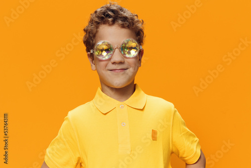a happy, joyful boy stands in a yellow T-shirt on a yellow background in bright masquerade glasses and smiles