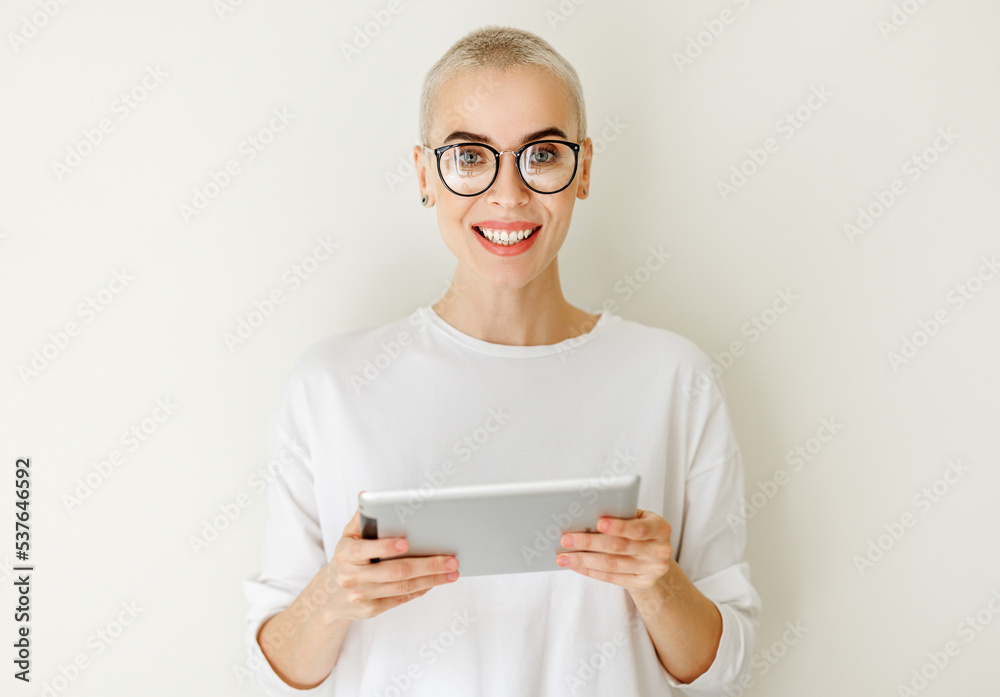Beautiful woman freelancer with very short hair holding tablet and looking at camera on blank wall