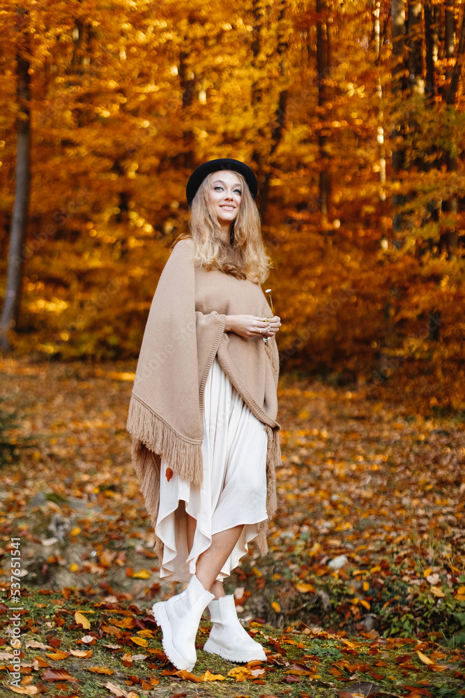 Happy and beautiful woman in a brown poncho in the middle of the autumn yellow forest.