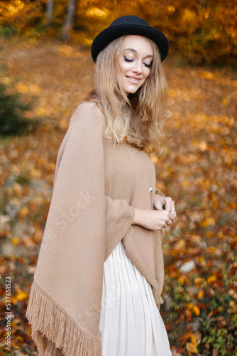 Happy and beautiful woman in a brown poncho in the middle of the autumn yellow forest.