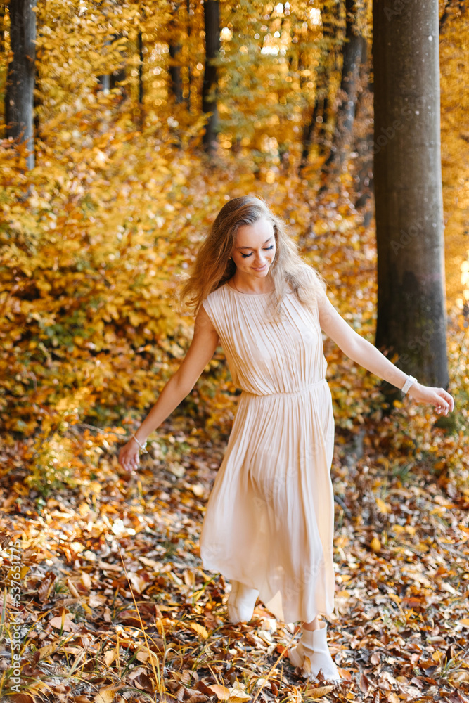 A playful woman walks in the autumn yellow forest against the background of a warm sunset.