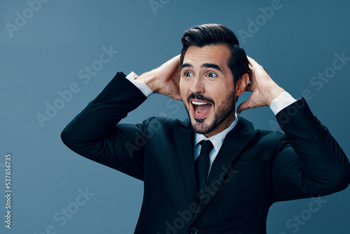 Business man happy smile with teeth open mouth raised hands up shouting surprise on blue background in business suit.