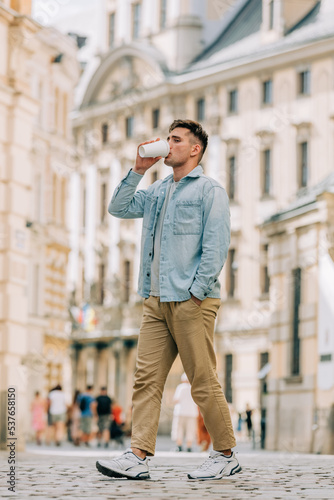 Stylish caucasian male with takeaway cup of coffee walking on the street of old town in Wroclaw, Poland