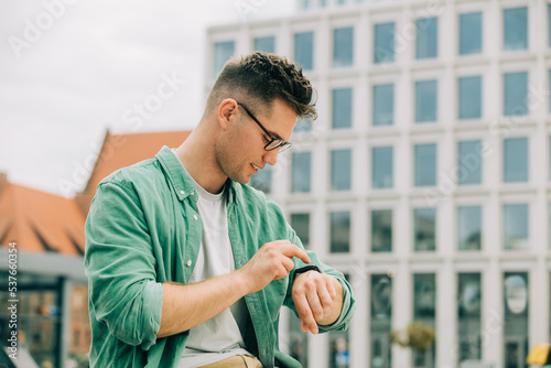 Εκτύπωση καμβά Stylish self-confident young guy in green shirt chech a time on watch on city st