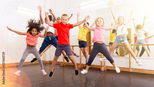 Group of cheerful tweens jumping with female trainer during modern dances class..