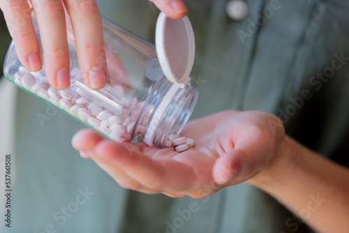 woman pours white pills from a transparent jar into her hand