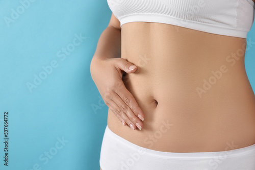 Woman in underwear touching her belly on light blue background, closeup. Healthy stomach