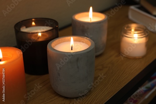 Lit candles in different holders on wooden table indoors