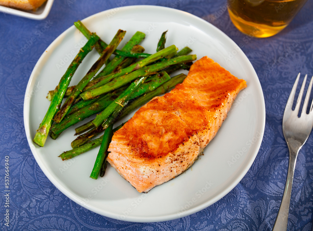 Tasty grilled salmon steak with asparagus garnish served on white plate