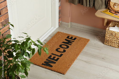 Door mat with word Welcome on wooden floor in hall photo
