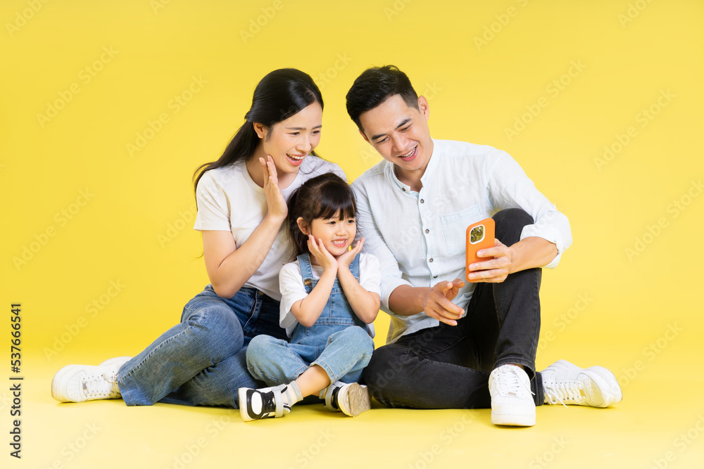 Image of Asian family sitting together happy and isolated on yellow background Image of Asian family sitting together happy and isolated on yellow background