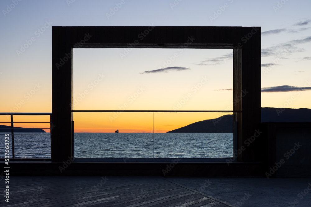 Observation deck on the sea coast. Scenic view of the sea bay at sunset. In the distance, on the horizon, a ship and mountains. Nagaev Bay, Sea of Okhotsk, Magadan, Magadan Region, Far East of Russia. Observation deck on the sea coast. Scenic view of the sea bay at sunset. In the distance, on the horizon, a ship and mountains. Nagaev Bay, Sea of Okhotsk, Magadan, Magadan Region, Far East of Russia.