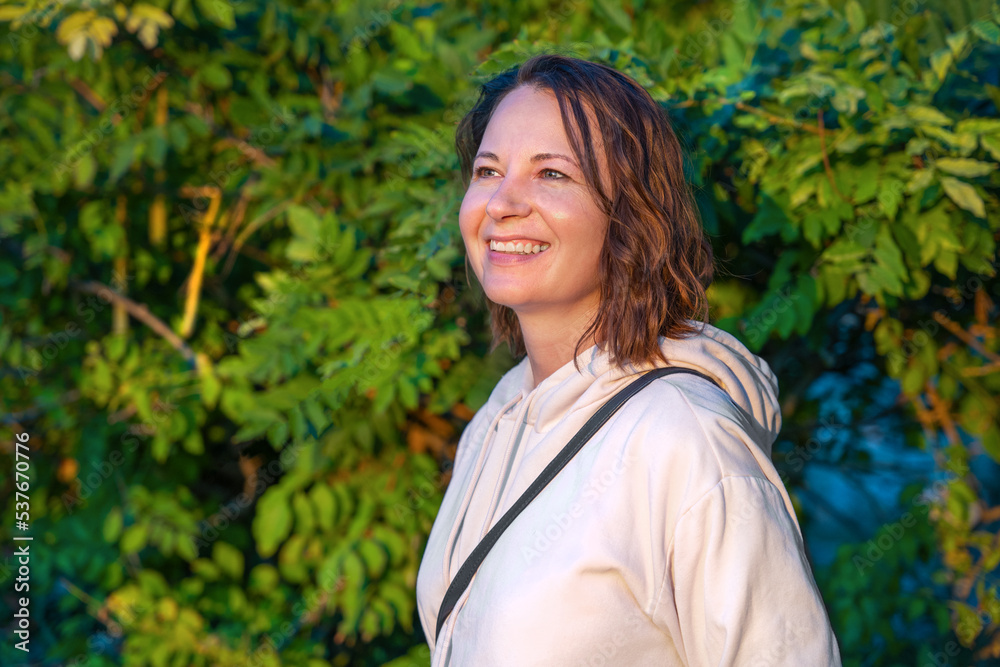 Happy woman with calm radiant face against background of tree leaves walks in park. Unity with nature fight stress positive energy, biophilia, mental calm conscious living in moment, taste of life Happy woman with calm radiant face against background of tree leaves walks in park. Unity with nature fight stress positive energy, biophilia, mental calm conscious living in moment, taste of life
