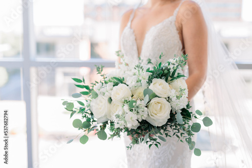 Bride is holding a white flower bouquet against her white wedding dress