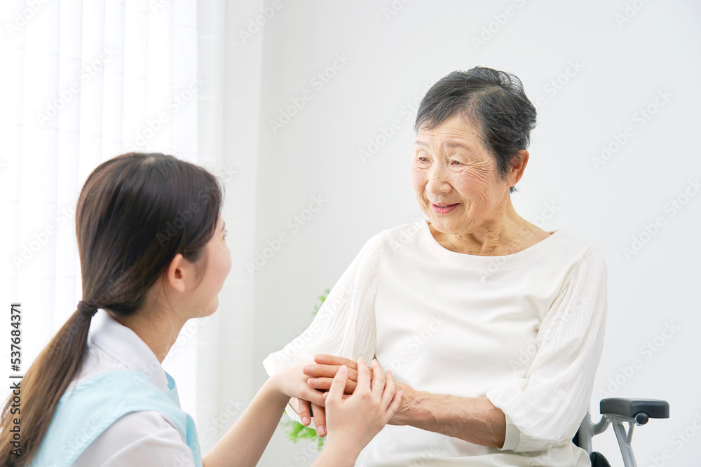 室内で車椅子に乗った高齢者女性と話す介護士 室内で車椅子に乗った高齢者女性と話す介護士
