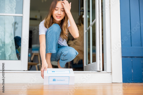 Close up hands of sick Asian woman sitting at door to receive medication first aid pharmacy box from hospital delivery service at floor home, merchandise medicine online business, healthcare concept