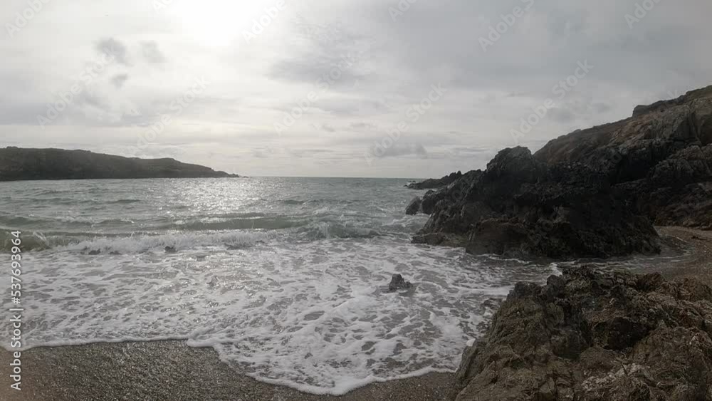 Slow motion peaceful ocean waves breaking against rugged Welsh coastline at sunrise Slow motion peaceful ocean waves breaking against rugged Welsh coastline at sunrise