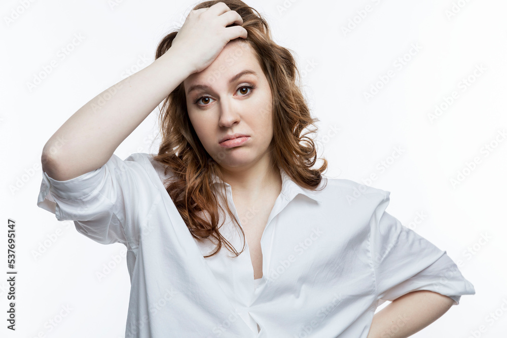 Tired young woman in a white shirt holds her head. Women's problems, depression and illness. White background. Tired young woman in a white shirt holds her head. Women's problems, depression and illness. White background.