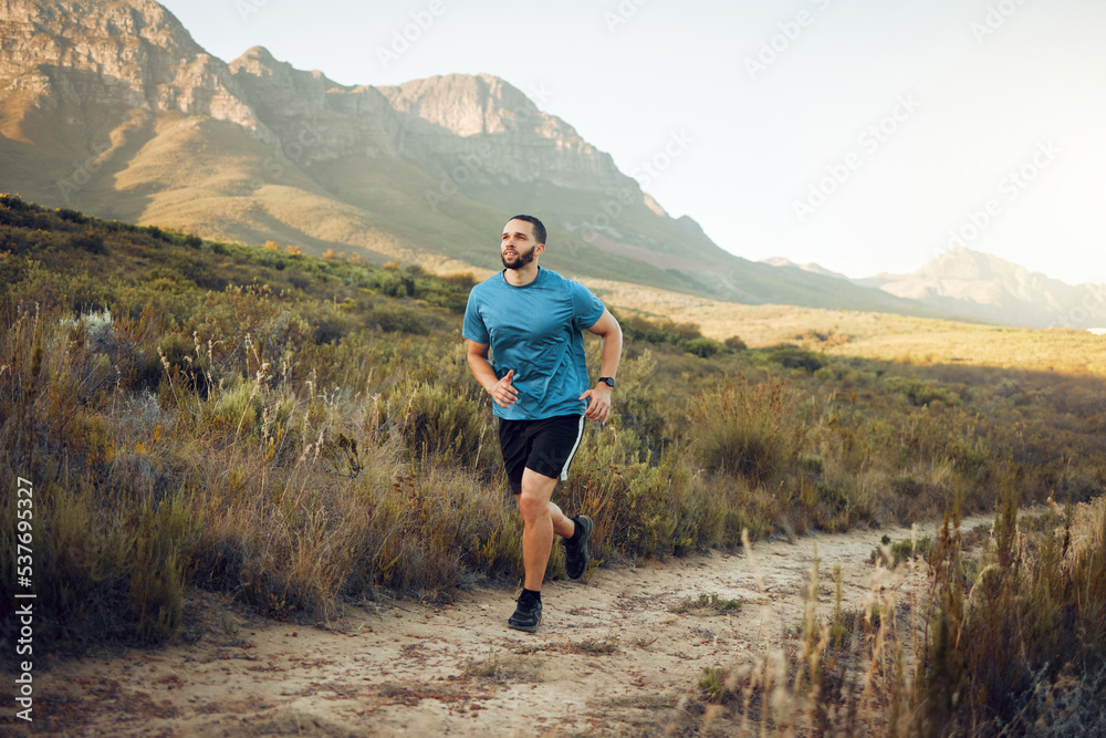 Health, mountain and man running in nature for fitness, training and sports exercise. Workout, wellness and summer with athlete runner in grass field path for peace, marathon and outdoor morning jog