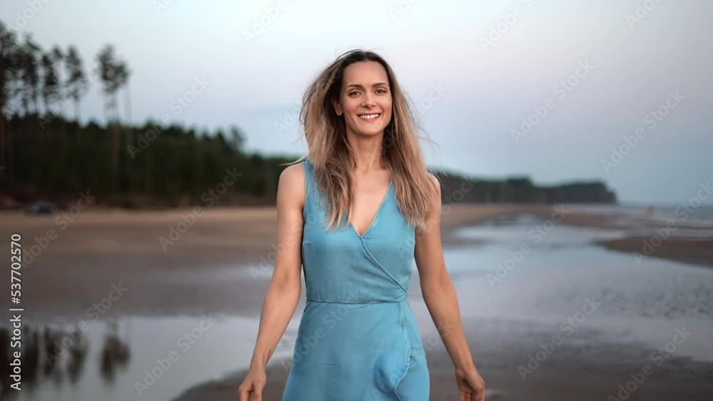 Beauty blonde woman in blue dress walking on evening beach summer nature seacoast slow motion Beauty blonde woman in blue dress walking on evening beach summer nature seacoast slow motion