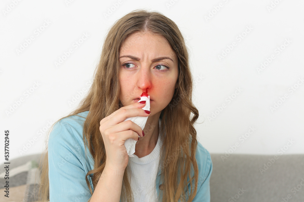 Young woman wiping nosebleed with tissue at home Young woman wiping nosebleed with tissue at home