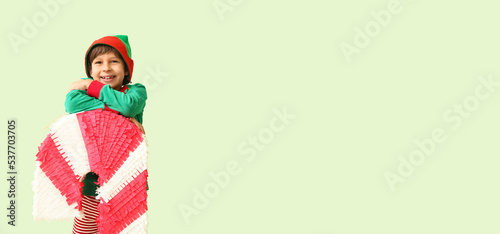 Cute little boy dressed as elf with candy cane pinata on light color background with space for text