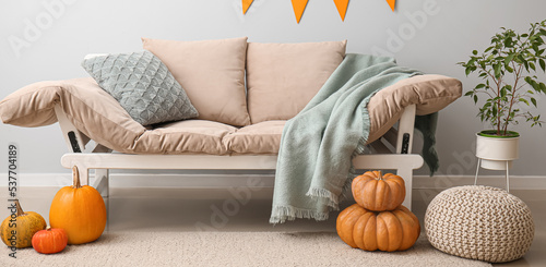 Interior of light living room with couch, Halloween pumpkins and pouf