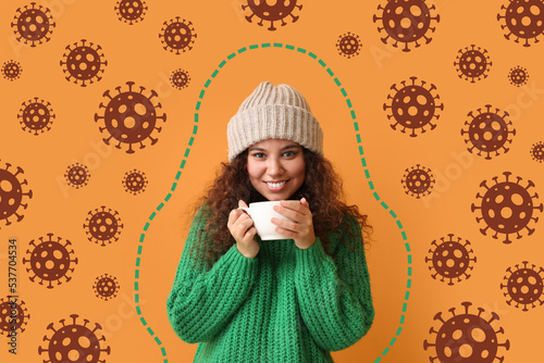 Happy young African-American woman with cup of hot tea and drawn virus on orange background. Concept of strong immunity