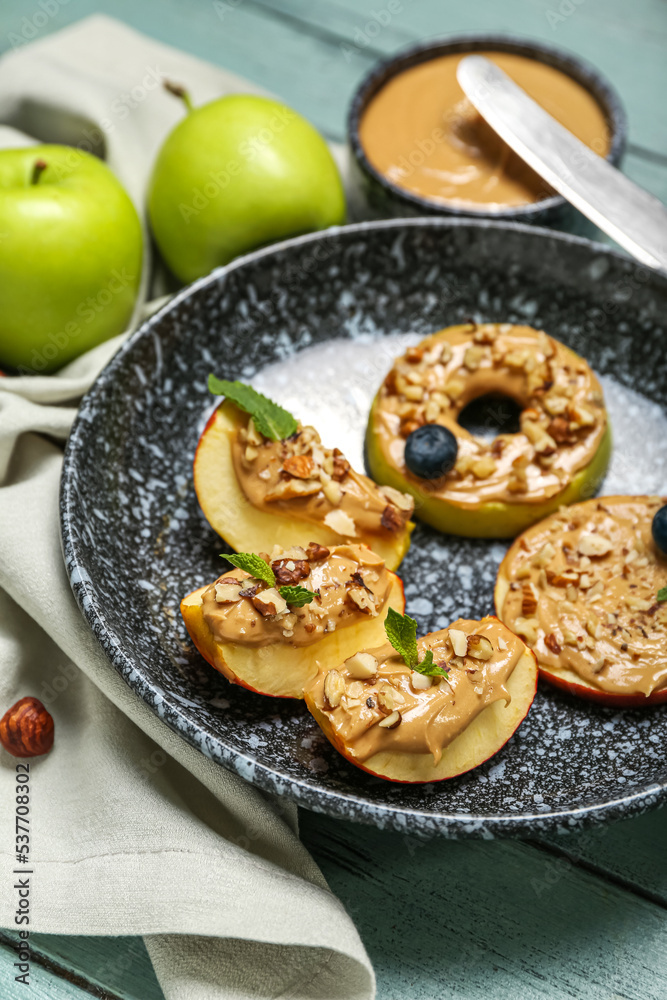 Plate of tasty apple wedges and rounds with nut butter on color wooden table, closeup