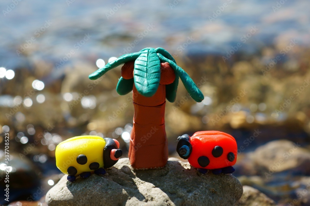 Two toy ladybugs and a palm tree on the background of the river. Bright sunny day. Vacation at the sea.