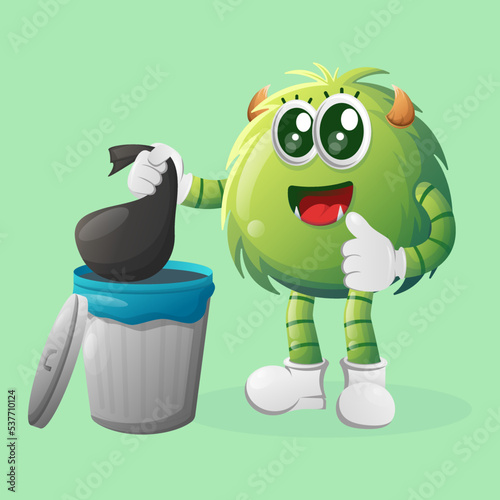 Cute green monster placing reusable waste into garbage can