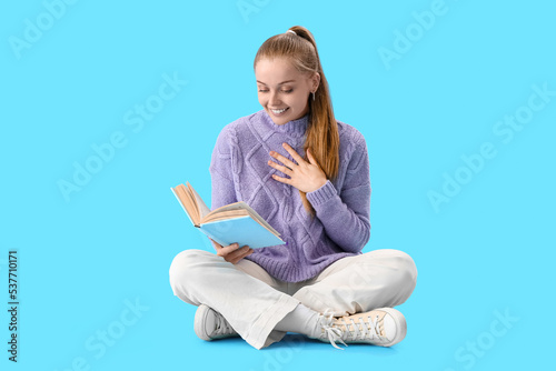 Happy young woman reading book on blue background