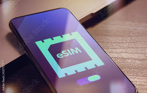 eSIM - Embedded SIM technology concept with smartphone very close lying on a wooden table with esim icon on the screen photo