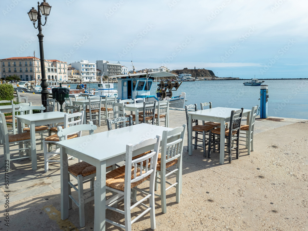 Greek outdoors tavern at port seaside Tinos island, Cyclades Greece. Chora town background.