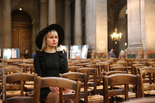 Woman in black dress and hat sits  in Catholic church. Widow prays alone photo
