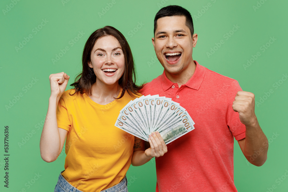 Young happy couple two friends family man woman wear basic t-shirt together hold in hand fan of cash money in dollar banknotes do winner gesture isolated on pastel plain light green background studio Young happy couple two friends family man woman wear basic t-shirt together hold in hand fan of cash money in dollar banknotes do winner gesture isolated on pastel plain light green background studio