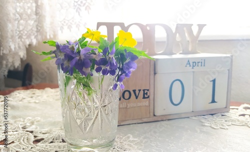 Spring flowers are purple and yellow. Flowers in a vase. Calendar. April first. Violets.