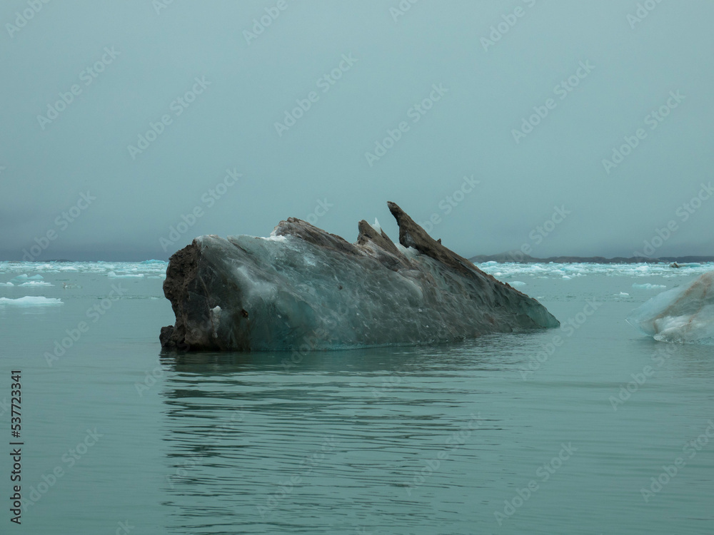 Dirty iceberg with sand and silt floating in the arctic ocean. Severely affected by global warming and climate change. Svalbard, Spitsbergen, Norway