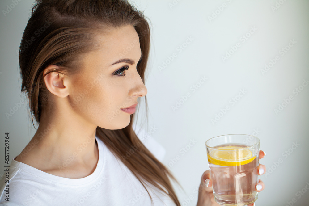 Beautiful young woman drinking fresh water with lemon at home Beautiful young woman drinking fresh water with lemon at home