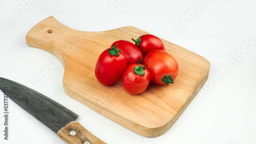 Pile of tomatoes on a wooden board and a knife next to it. Ripe tomatoes with cut lines. Organic fresh tomatoes isolated on white.