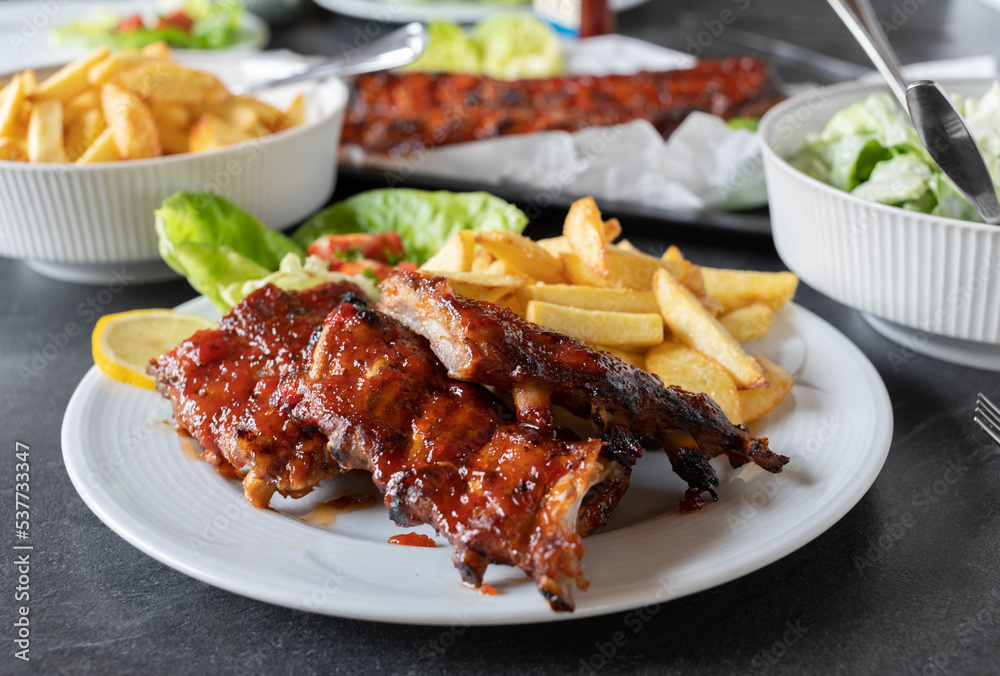 Plate with homemade barbecue pork ribs, french fries and salad on a dining table