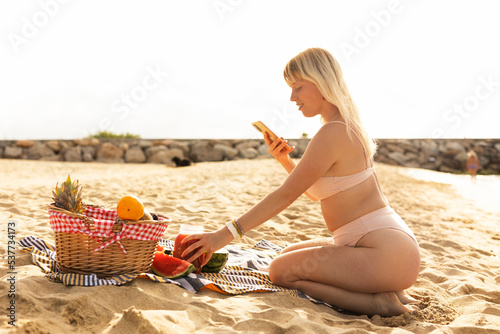 Cheerful young woman enjoy at tropical sand beach. Young woman taking a picture of fruit on the beach photo