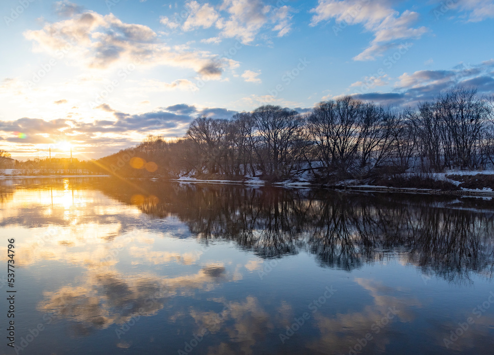 Winter landscape with river and trees at sunset.
