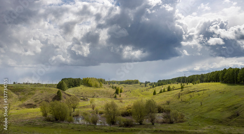 Spring landscape, dramatic sky over green hills before rain. The sun through the clouds illuminates the green meadows and ravines.