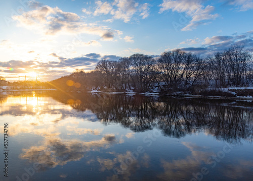 Winter landscape with river and trees at sunset.