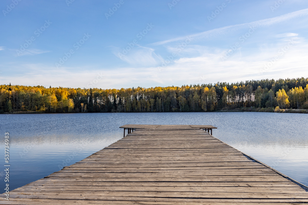 Obraz premium Wooden deck near the water. Sunny autumn day near the pond.