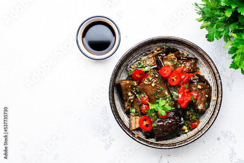 Grilled spicy eggplant with hot red chili peppers, soy sauce, garlic and sesame seeds in asian style, white table background, top view photo