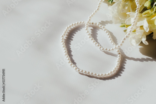 White bracelets with pearl beads on a white background with flowers.