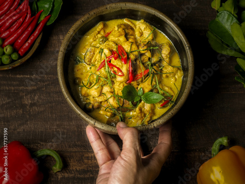 A women right hand serve a chicken green curry on a wood table