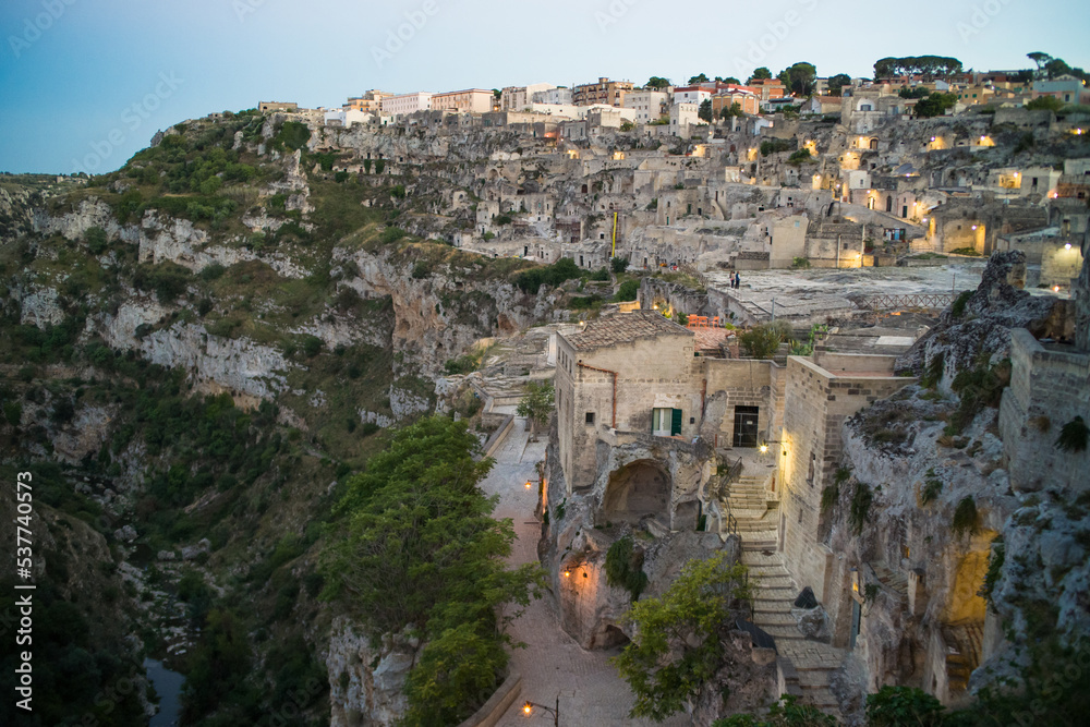 view after dark of old stone houses and churches on the slopes of the gorge in the historic center of the old town of Matera illuminated by street lamps. Cascade buildings of the old town with rocks 
